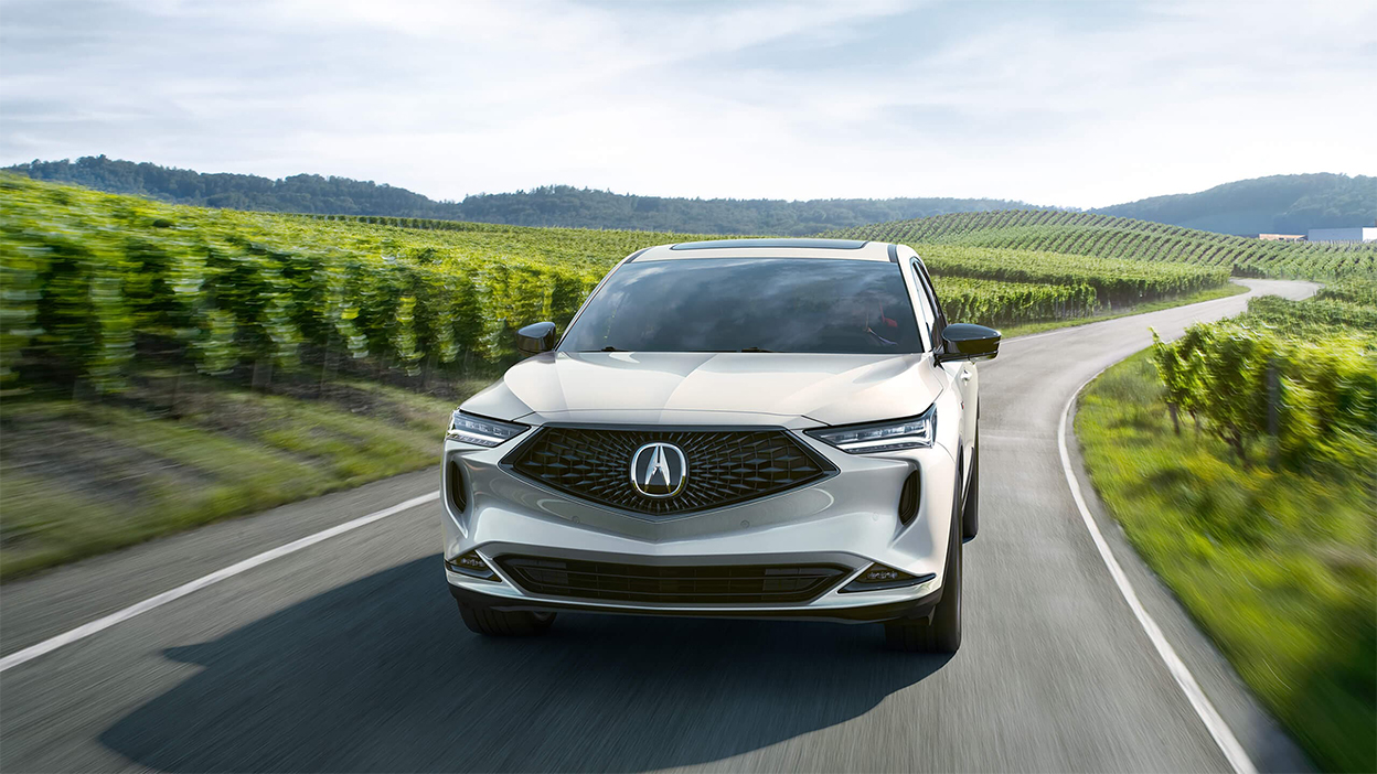 A grey MDX driving down a country road, passing by rows of grapevines.