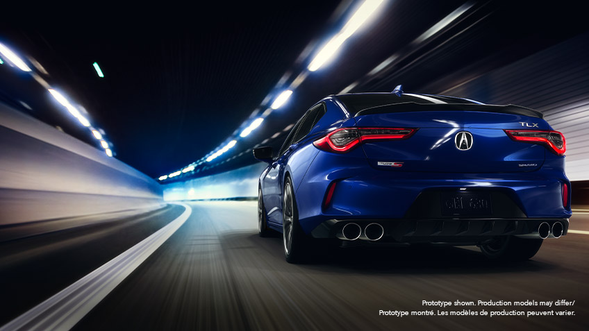 Rear view of a blue Acura TLX driving down a roadway at night, surrounded by city lights blurred by motion. Vue arrière d’une Acura TLX bleue roulant à pleine vitesse la nuit sur une route bordée de néons.